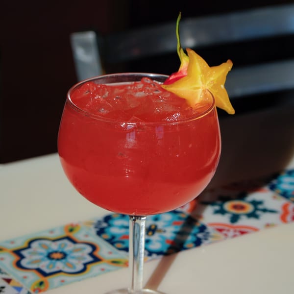 A vibrant red cocktail with ice and a star fruit garnish sits on a patterned table runner.