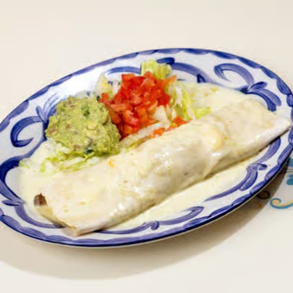 A cheese-covered burrito with guacamole, diced tomatoes, and shredded lettuce on a decorative plate.