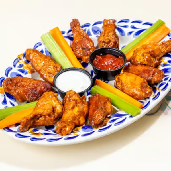 A platter of buffalo wings with celery, carrots, ranch, and hot sauce on a white and blue plate.