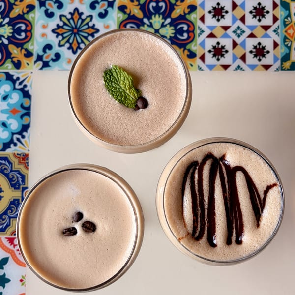 Three creamy coffee cocktails, one with mint, one with coffee beans, and one with chocolate drizzle.