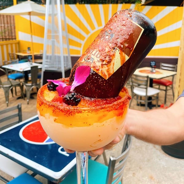 A large margarita with an inverted beer bottle, garnished with blackberries and a pink flower.