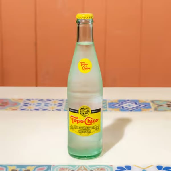 A bottle of Topo Chico sparkling mineral water on a white table with colorful tiles.