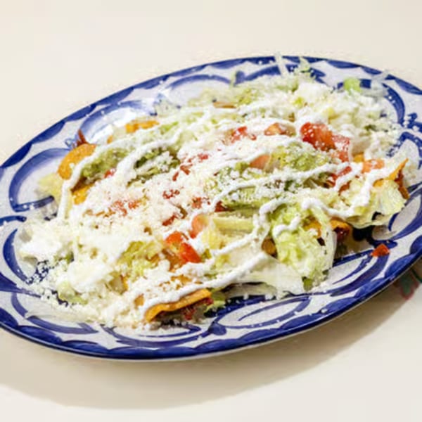A blue and white patterned plate filled with taquitos, topped with lettuce, tomatoes, cheese, and crema.