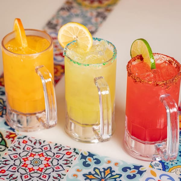 Three colorful margaritas, orange, yellow, and red, garnished with fruit slices and salt rims.