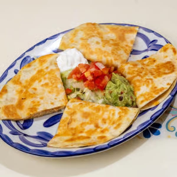 Four quesadilla wedges with guacamole, sour cream, and pico de gallo on a blue and white plate.
