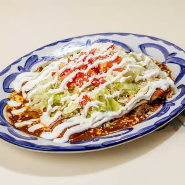 A plate of enchiladas topped with red sauce, lettuce, tomatoes, and sour cream.