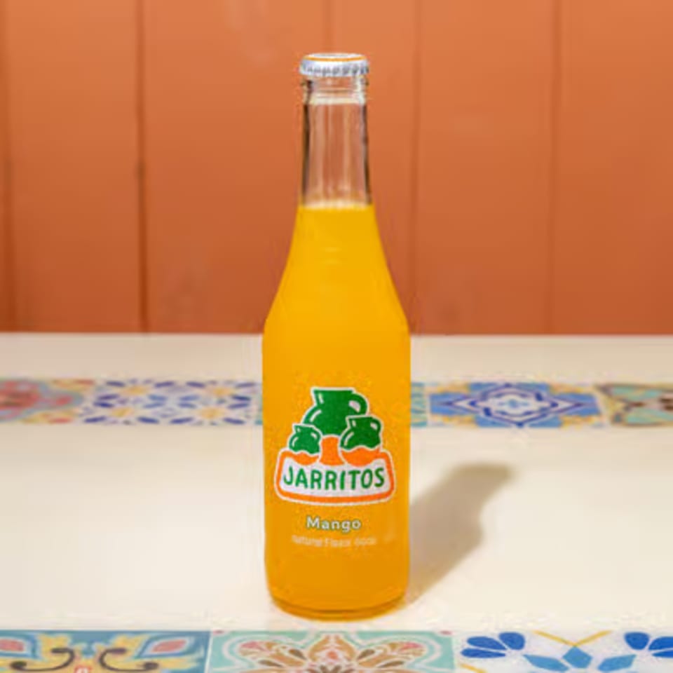 A bottle of Jarritos Mango soda on a white tiled surface with an orange background.