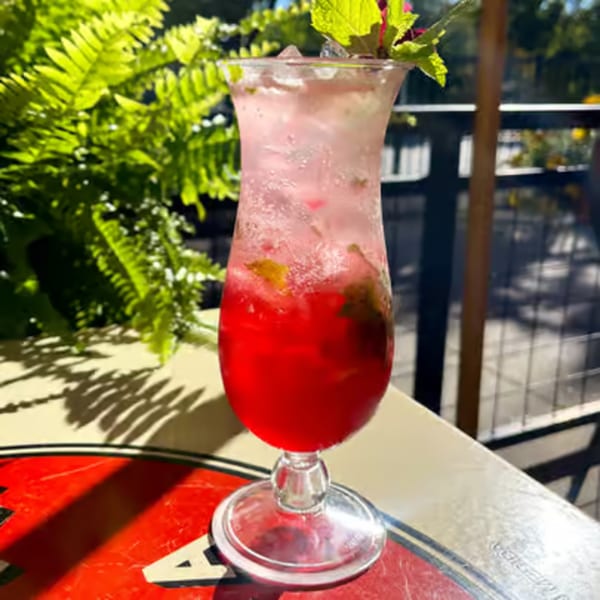A vibrant red and pink cocktail with mint and ice sits on a patterned table outdoors.