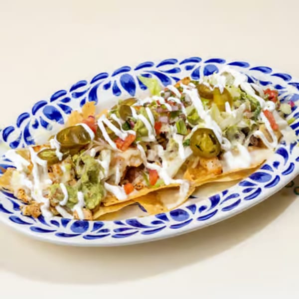 Chicken nachos with guacamole, sour cream, jalapeños, and pico de gallo on a decorative blue and white plate.