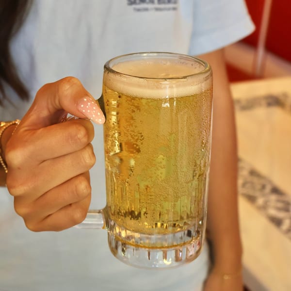 A hand with pink polka-dotted nails holds a frosty mug of golden beer with a foamy head.